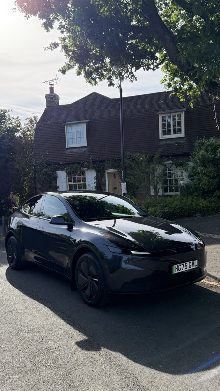 Stealth Grey Model Y RWD front three-quarter by a cottage